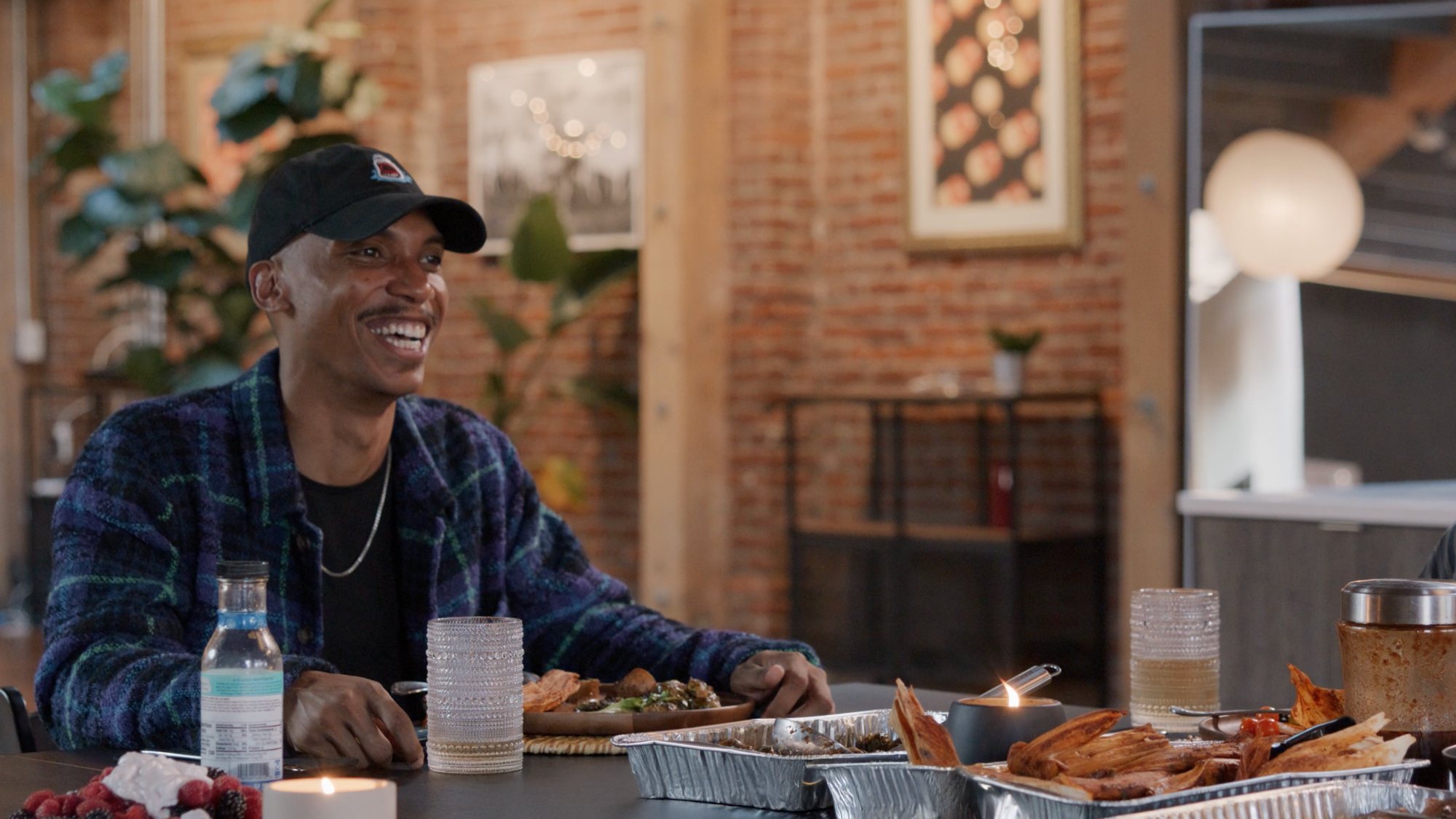 A man laughing at a dinner table in a brick-walled loft