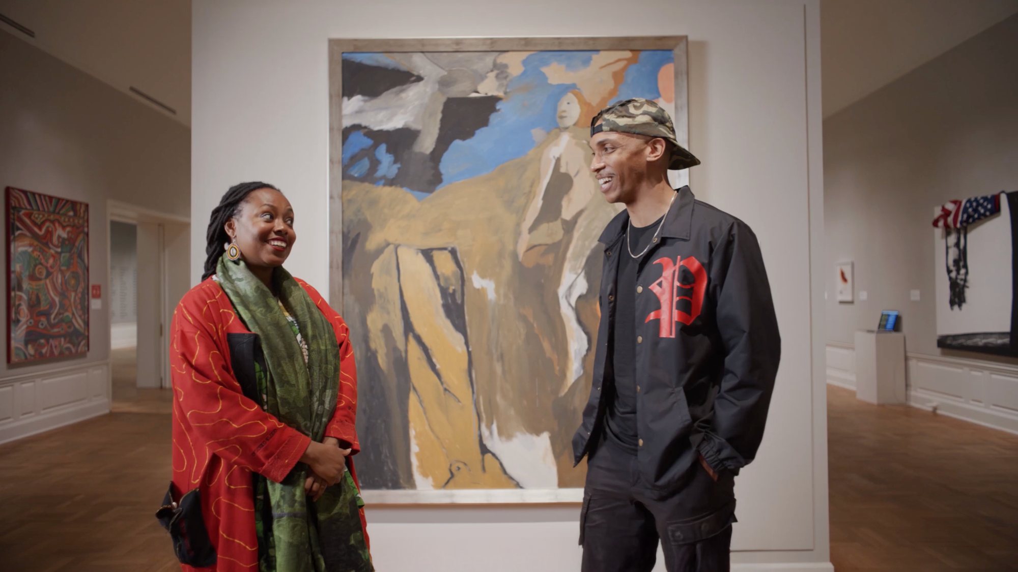 Two people talking in front of a large painting in a museum gallery