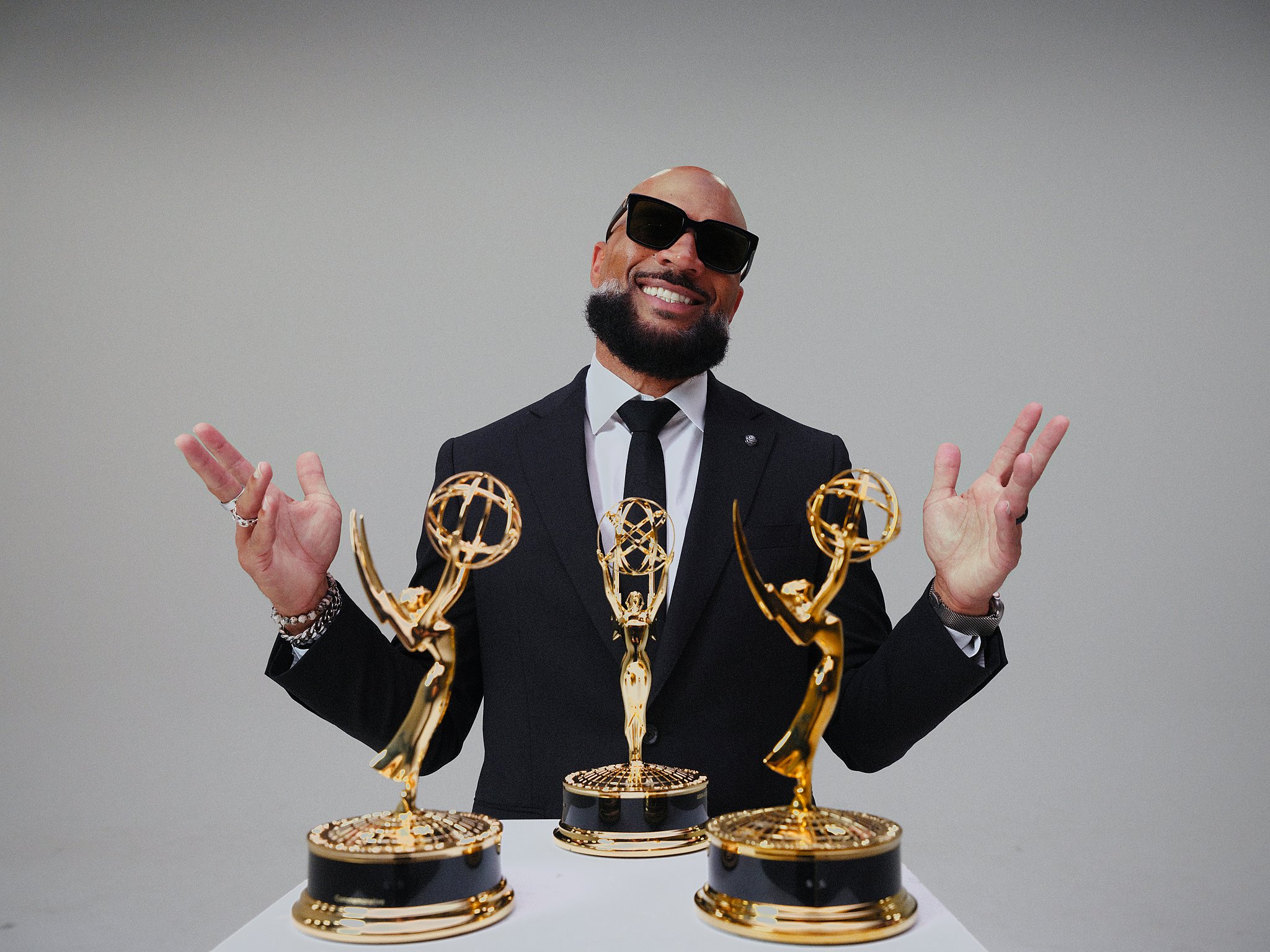 Rashad Floyd raising his arms behind three Emmy statuettes