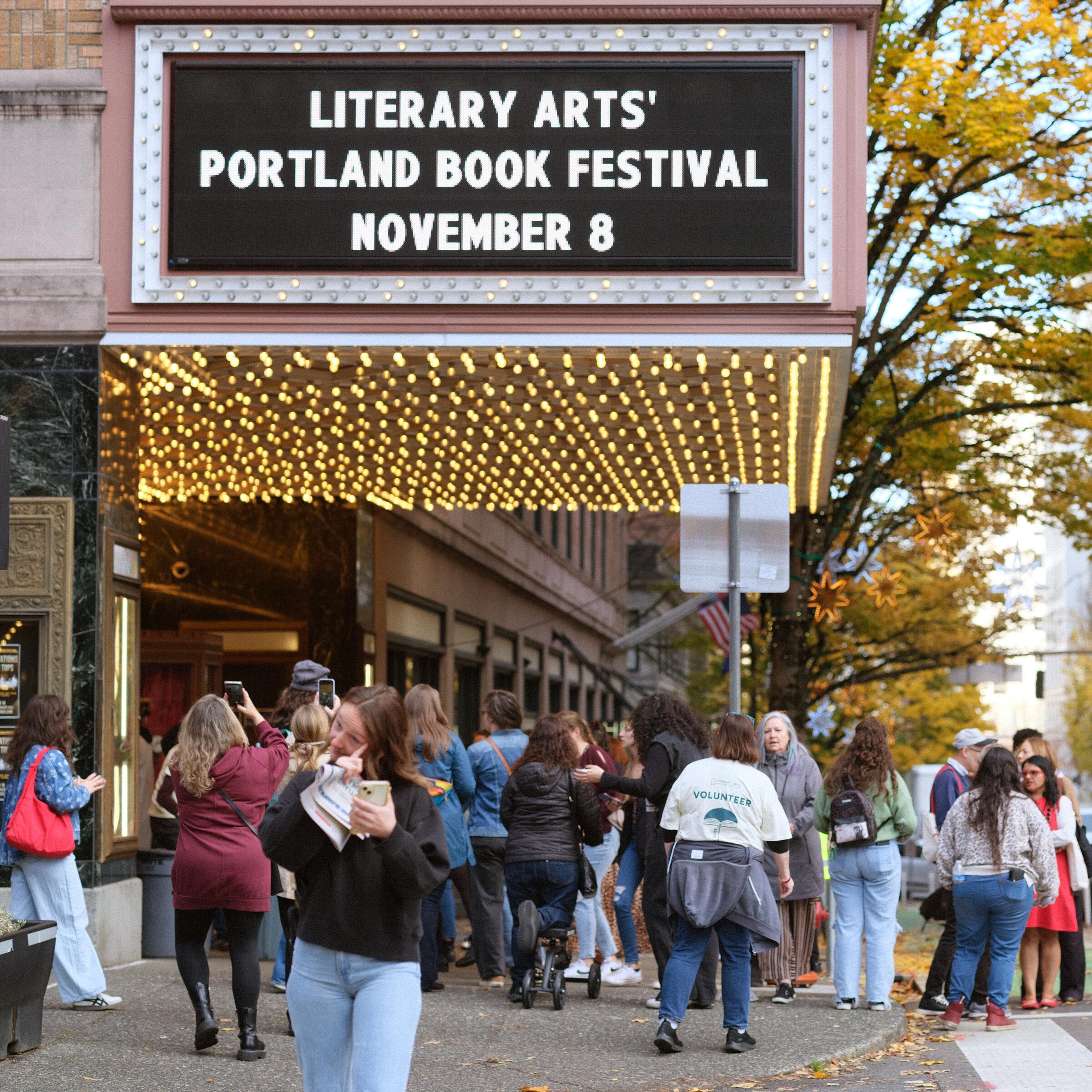 Portland Book Festival marquee glowing over the street crowd at dusk