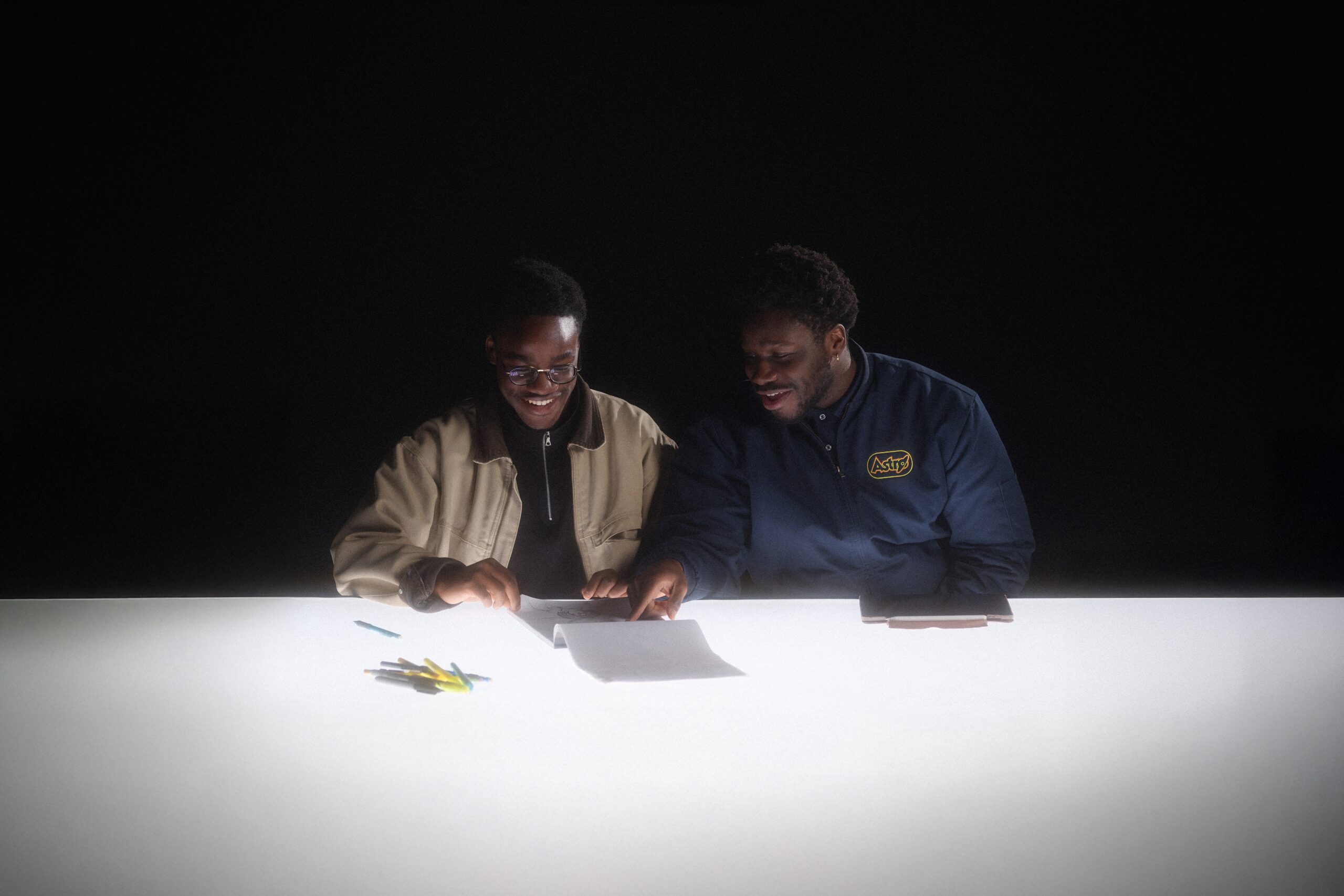 Two subjects reviewing papers on a brightly lit table in a dark studio