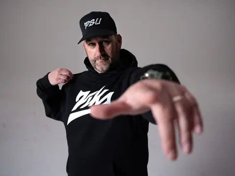 PSU coach in a black Vika hoodie reaching his hand toward the lens