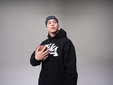 Player in a black Vika hoodie and skull cap holding a football, looking off camera