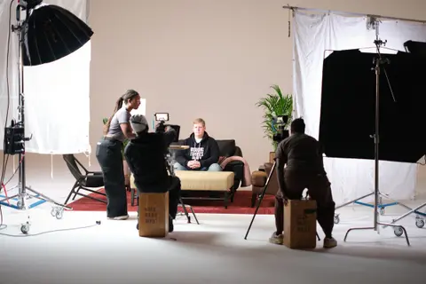 Wide behind-the-scenes view of a crew setting up an interview on a white studio cyc