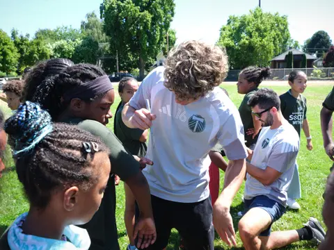 Kids crowding around a Portland Timbers player signing autographs on a grass field