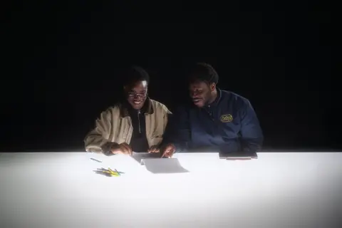 Two subjects reviewing papers on a brightly lit table in a dark studio