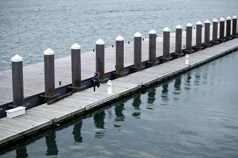 High wide view of a runner in a blue jacket running along a Boston harbor dock lined with pilings